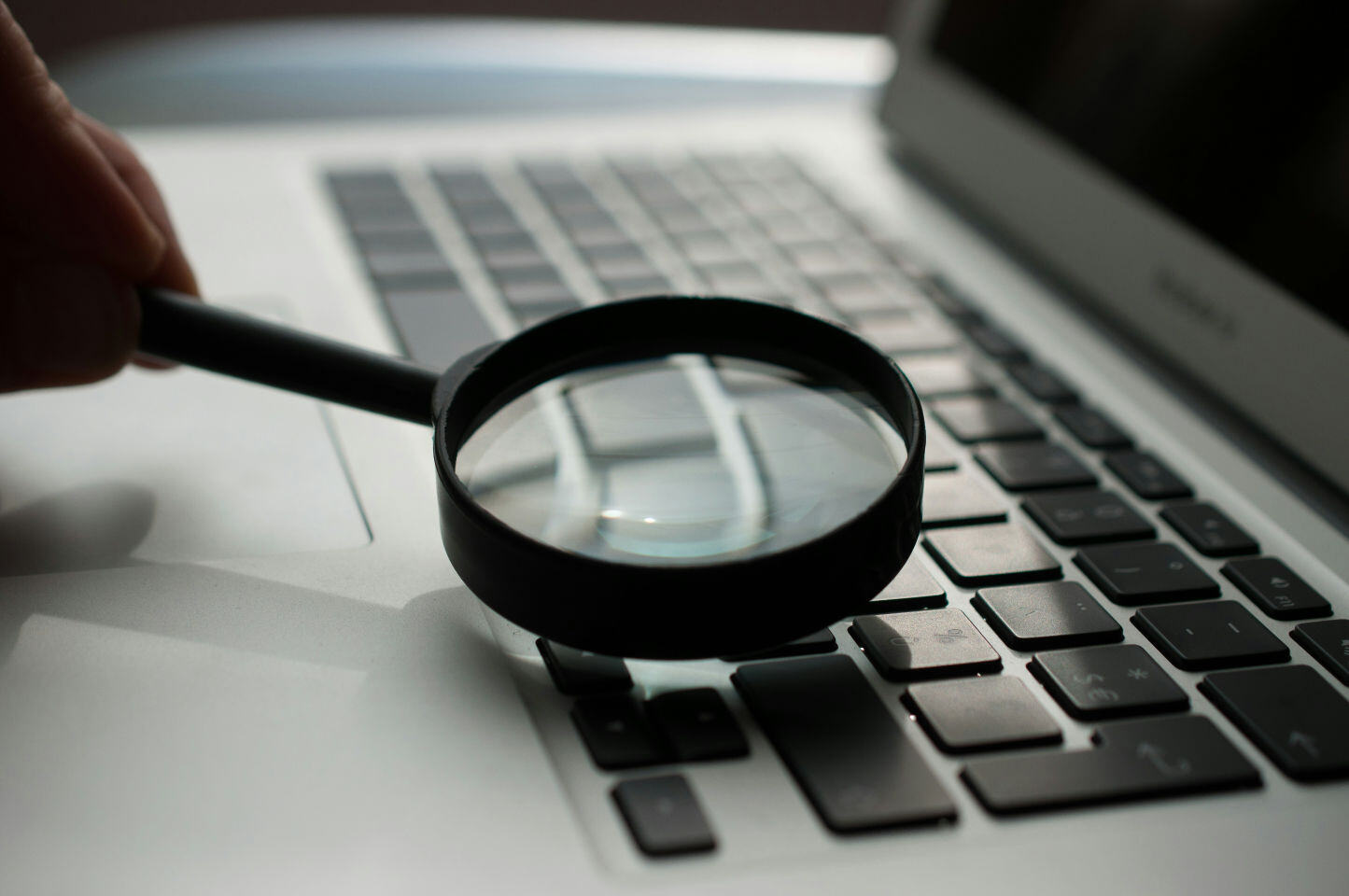 Magnifying glass over a laptop keyboard, representing cyber security management.